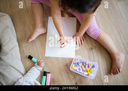 Paesaggio immagine di una bambina in vestiario rosa seduta su un pavimento di legno e fare somme su un foglio di carta con un textmarker rosa e cotto colorato Foto Stock