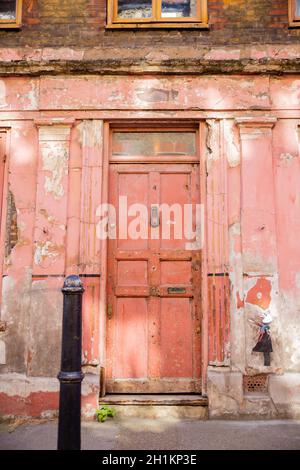 Ritratto Vista di una porta rossa deteriorata su un edificio con una bambina dipinta su un muro Foto Stock