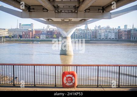 Vista del paesaggio da sotto il Millenium Bridge con il Tamigi sottostante e un Orange Emergency Floaty lungo un trafficato percorso fluviale a Londra, Regno Unito Foto Stock