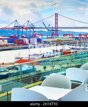 Vista porto commerciale di Lisbona dalla terrazza ristorante all'aperto, container, gru merci, motoscafi, binari ferroviari e parcheggio auto, ponte 25 aprile Foto Stock