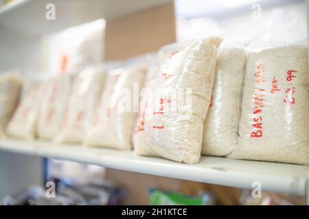 Foto di riso confezionato in sacchetti di plastica e su una mensola Pronto per la vendita con i prezzi scritti sulle borse Foto Stock