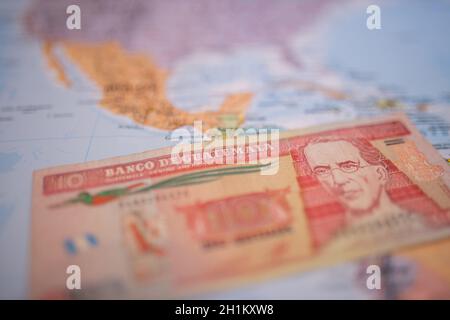 Primo piano di una banconota da dieci quetzales guatemaltechi - con le parole Banca del Guatemala in spagnolo - sotto il Guatemala su una mappa colorata e sfocata di Foto Stock