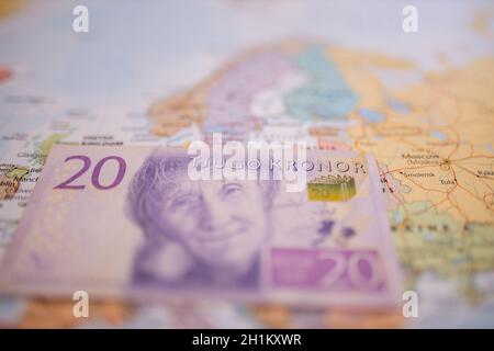 Primo piano di una banconota da venti corone svedesi - con le parole Twenty Kronor in svedese - sotto la Svezia su una mappa europea colorata e sfocata Foto Stock