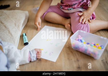 Paesaggio immagine di una bambina in abiti rosa facendo somme su un foglio di carta con palline di cotone colorate, come lei punta e si siede sul pavimento di legno Foto Stock