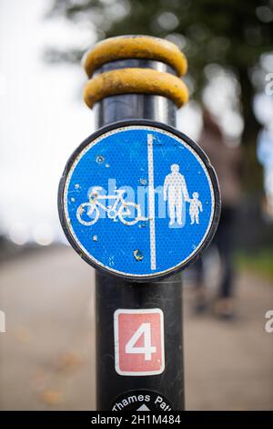 Cartello rotondo blu su palo con immagini di persone e una bicicletta che indica i sentieri pedoni e ciclisti. Segnaletica stradale con strada sfocata come sfondo. Foto Stock