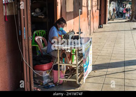 Bangkok, Thailandia - 7 dicembre 2019: Marinaio di strada femminile che fa vestiti con la vecchia macchina da cucire sul negozio di riparazione veloce di abbigliamento di strada a Bangkok, Foto Stock