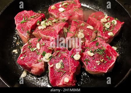 Costolette di agnello friggere su una padella di ghisa con aglio e rosmarino. Foto Stock