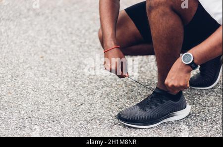 Primo piano Asian sport Runner uomo nero indossare orologio seduta lui cercando scarpe da running scarpe da running scarpe ottenere pronti per jogging e correre al heal strada all'aperto guarire Foto Stock