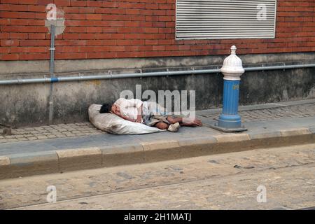 Un uomo senza tetto si trova addormentato sul marciapiede fuori dalla trafficata stazione ferroviaria di Kolkata, India Foto Stock