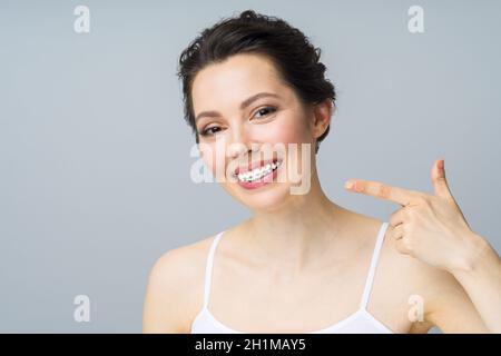 Una giovane donna con bretelle sui denti, sorride e punta allo spazio della copia con un gesto della mano, Foto Stock