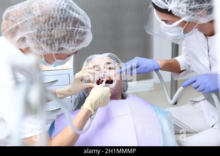 Il dentista e l'assistente effettuano la pulizia dentale professionale e l'igiene orale. Prevenzione di carie e malattie gengivali. Riavvolgitore in bocca. Top vi Foto Stock