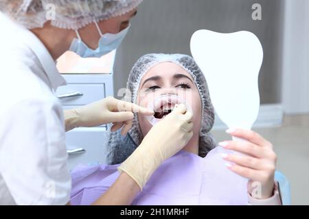 Un dentista fa una pulizia professionale dei denti per una ragazza giovane. Il paziente guarda nello specchio. Prevenzione della carie. Il concetto di salute. Vista dall'alto Foto Stock