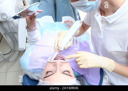 Un dentista fa una pulizia professionale dei denti per una ragazza giovane. Spazzolino elettrico nelle mani del medico. Il paziente guarda nello specchio. Preve Foto Stock