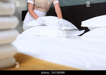 Una cameriera in uniforme cambia la biancheria da letto in una camera d'albergo costosa. Pulite gli asciugamani sul letto. Il concetto di servizio di qualità nell'hotel. Hotel business. O Foto Stock