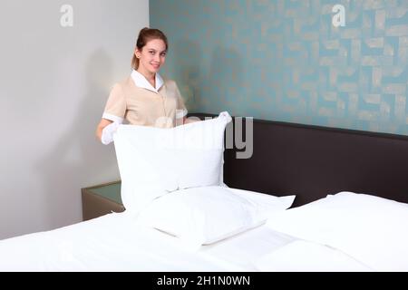 Una cameriera in uniforme cambia la biancheria da letto in una camera d'albergo costosa. Mani in guanti di cotone bianco. La ragazza sorride e tiene un cuscino nelle sue mani . Il con Foto Stock