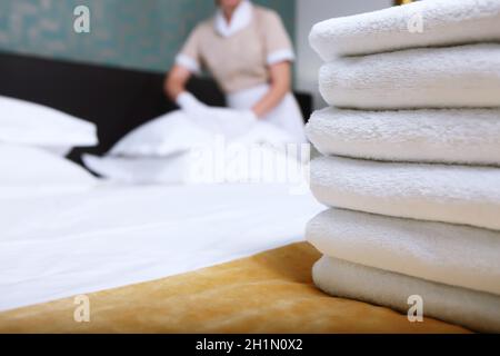 Una cameriera in uniforme cambia la biancheria da letto in una camera d'albergo costosa. La persona è fuori fuoco. Pulite gli asciugamani sul letto. Il concetto di servizio di qualità in Foto Stock