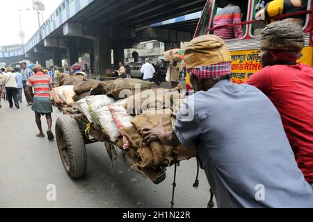 Gli indiani che lavorano duramente spingono carichi pesanti attraverso le strade di Kolkata, India Foto Stock