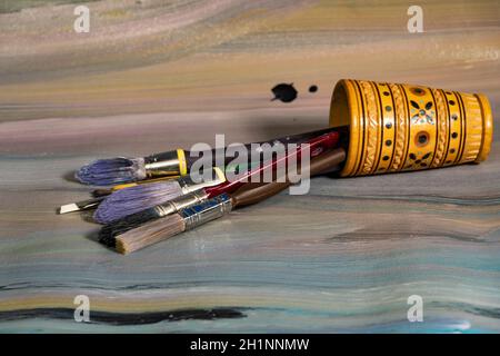 Spazzole per la pittura in una cassa di legno a matita su cui giace una vecchia tela dipinta con vernici ad olio Foto Stock