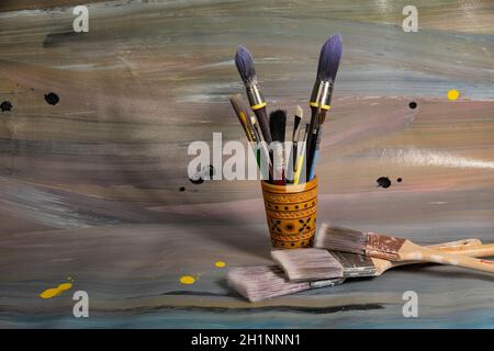 Spazzole per la pittura in una cassa di legno a matita su cui giace una vecchia tela dipinta con vernici ad olio Foto Stock