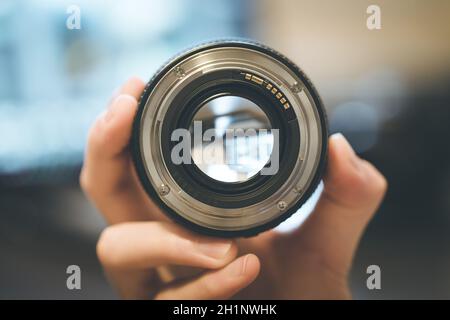 Fotografo detiene una foto professionali ottica in mano. Laptop in uno sfondo sfocato. Foto Stock