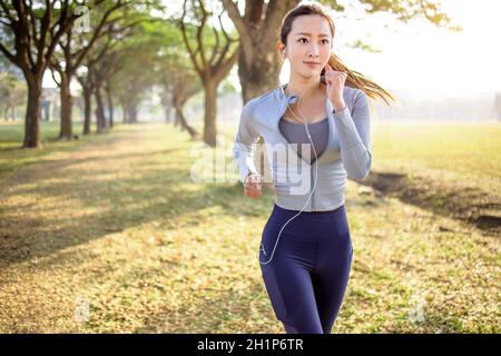 Bella giovane donna asiatica che corre nel parco al mattino Foto Stock