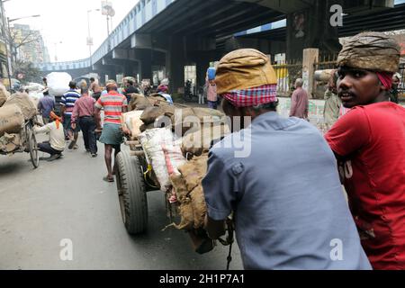 Gli indiani che lavorano duramente spingono carichi pesanti attraverso le strade di Kolkata, India Foto Stock