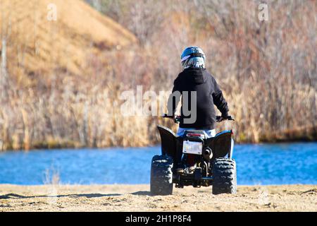 La parte posteriore di un ragazzo su un quad con uno stagno blu sullo sfondo. Foto Stock