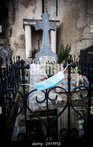 ESPELETTE, FRANCIA - CIRCA GENNAIO 2021: Maschera chirurgica blu attaccata alla griglia intorno ad una tomba. Foto Stock