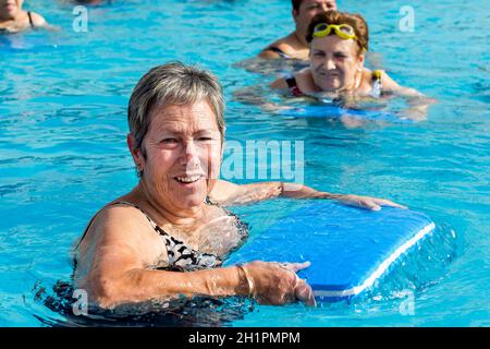 Primo piano ritratto di donna anziana che fa l'acqua esercizio con asse di calci nella piscina all'aperto. Foto Stock