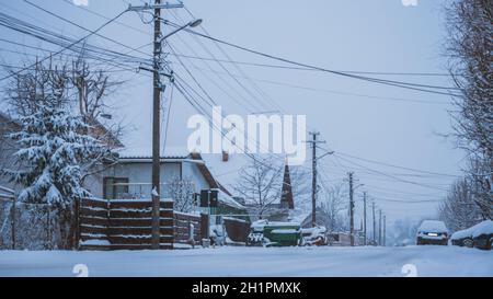 Angolo di visuale basso della strada innevata con case, automobili e pali di luce in Romania Foto Stock