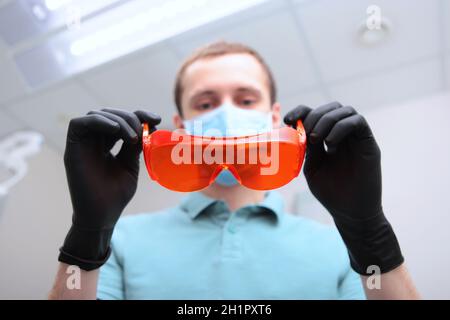 Il dentista indossa occhiali di sicurezza di colore arancione. Foto irriconoscibile. L'uomo è fuori fuoco. Spazio di copia. Foto Stock