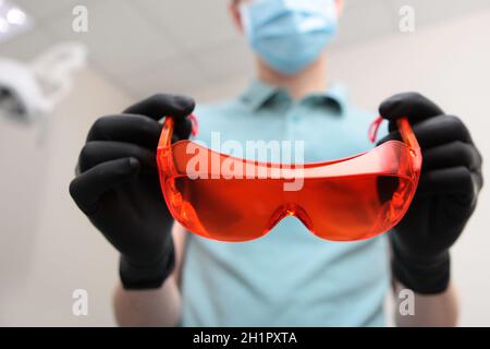 Il medico dentista indossa guanti e indossa occhiali di sicurezza di colore arancione. Foto irriconoscibile. Spazio di copia. Foto Stock