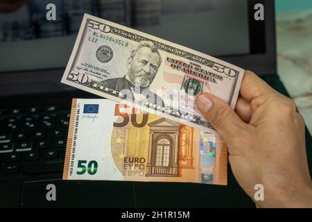 Una mano che detiene due banconote, una di cinquanta dollari americani e l'altra di cinquanta euro Foto Stock