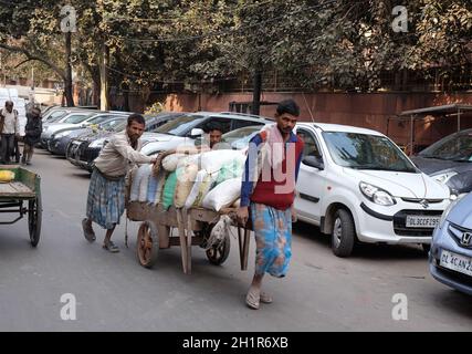 Gli indiani che lavorano duramente spingono carichi pesanti attraverso le strade di Delhi, India Foto Stock