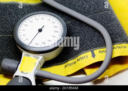 uno sfigmomanometro portatile poggiato su un bracciale giallo per adulti con chiusura in velcro. Strumento per la misurazione della pressione sanguigna. Scala graduata con p Foto Stock
