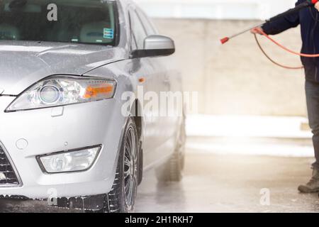 Lavarsi l'auto con acqua e sapone in autolavaggio. Uomo con pulitore ad alta pressione per la pulizia esterna del suo veicolo argentato. La mainta dell'automobile senza contatto Foto Stock