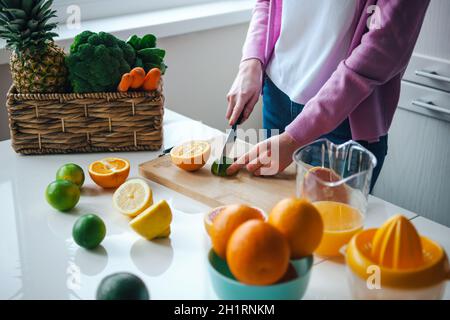 Vista ravvicinata delle mani femminili che tagliano le fette di lime in modo da poterli mettere nel succo del mattino Foto Stock