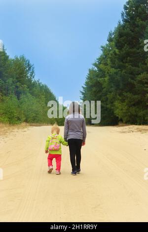 Piccoli turisti vanno su strada. Le bambine che viaggiano camminano sul sentiero forestale, le sorelle dei piccoli viaggiatori si recano sulla strada sabbiosa che tiene le mani. Bambini nella foresta Foto Stock