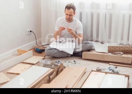 Uomo auto-assemblaggi mobili in legno a casa senza padrone. Leggere le istruzioni. Concetto DIY. Foto Stock