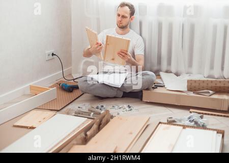Uomo auto-assemblaggi mobili in legno a casa senza padrone. Leggere le istruzioni. Uomo che legge le istruzioni. Concetto DIY Foto Stock