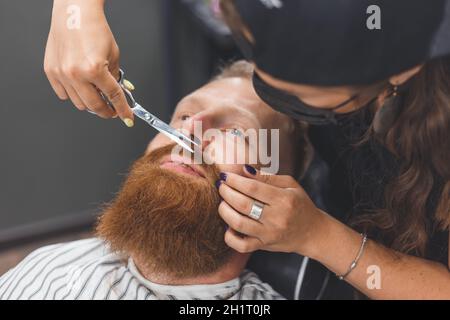 Un uomo in un barbiere. Baffi da taglio per barbiere donna. Barbiere donna in maschera Foto Stock