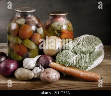 Su uno scaffale nel seminterrato sono due vasetti di vetro di pomodori in scatola, cetrioli e peperoni. Sigillato con un coperchio ermetico. Un certo numero di verdure fresche. FR Foto Stock