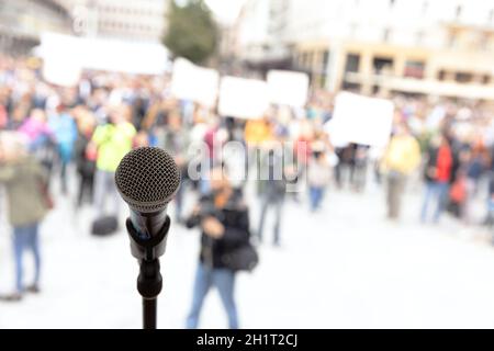Manifestazione pubblica o protesta politica. Microfono a fuoco contro una folla irriconoscibile di persone. Foto Stock