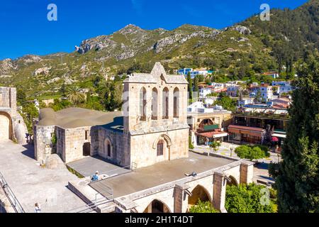 Abbazia medievale di Bellapais con villaggio sullo sfondo. Famosa attrazione turistica costruita da Canons regolare nel 13 ° secolo. Distretto di Kyrenia, Cypr Foto Stock