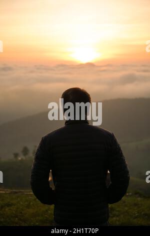 uomo che guarda l'alba da solo in cima alla collina Foto Stock