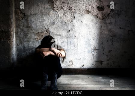 Donna depressa e solitaria seduta da sola in una camera vecchia sporca e spaventosa abbandonata sul pavimento di legno che si sente miserabile e ansiosa piangere sulla sua vita, depr Foto Stock