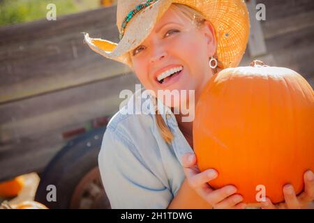 Bella Donna bionda Rancher indossando il cappello da cowboy detiene una zucca in un rustico di impostazione per il paese. Foto Stock