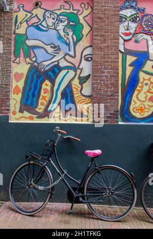 Bicicletta dall'aspetto classico parcheggiata sotto un moderno dipinto di uomo e donna che danzano. La bici pende contro il muro di mattoni con bellissimi e colorati murales. Mod Foto Stock