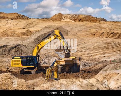 Falda terra gialla che riempie un autocarro in un cantiere Foto Stock