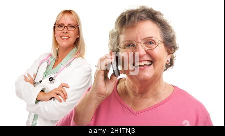 Donna anziana felice usando il telefono delle cellule con il medico femminile o infermiera dietro isolato su uno sfondo bianco. Foto Stock